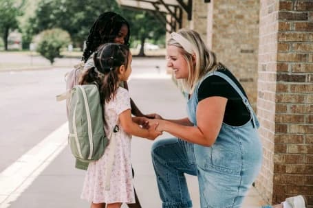Parent crouched at a school gate helping with afternoon pickup
